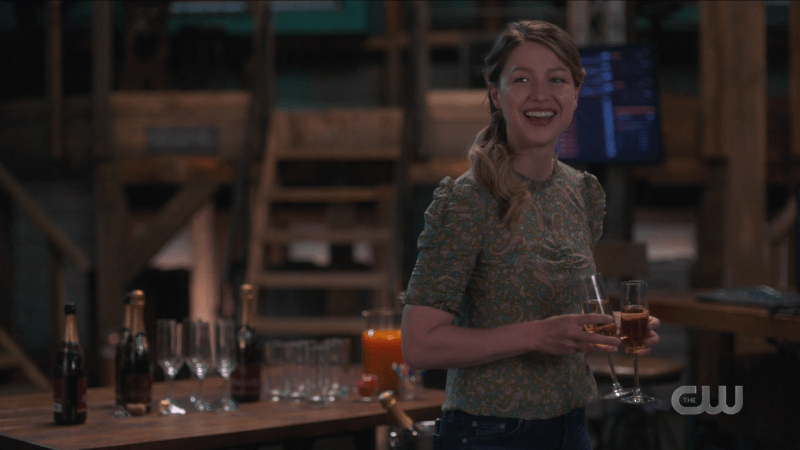 Kara beams at Lena with two glasses of champagne in her hands