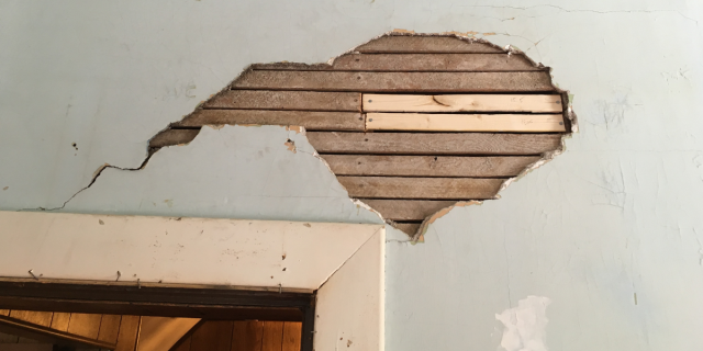 A look at a piece of wall above a doorway. A good chunk of plaster has fallen away revealing the lath. Two pieces of lath are a much brighter color than the other lath indicating their newness.
