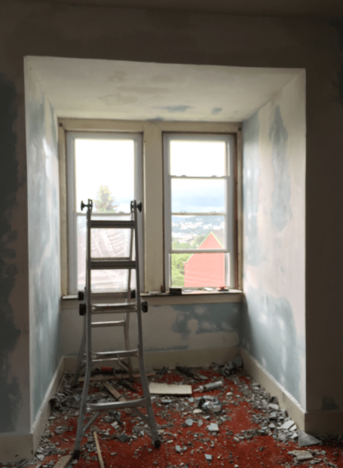 A mostly patched, sanded and repaired nook. The plaster is reattached and repaired. There is visible patching everywhere and debris across a red carpet.