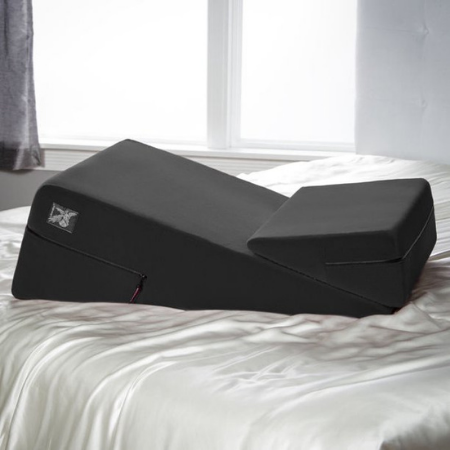 A black Liberator pillow, which looks like a ramp-shaped cushion, is on a white bed
