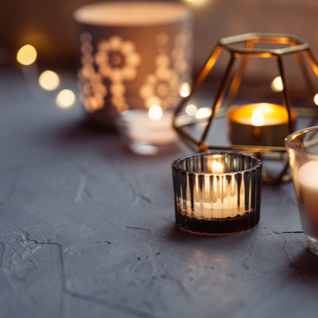 An array of candles in different candle holders and sparkling lights are on a grey surface