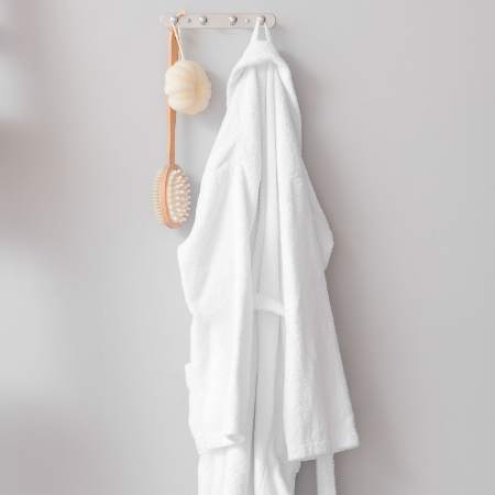 A white robe hanging on a hook beside a loufa and body brush