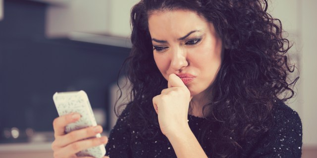 A woman with curly brown hair is looking at her phone with a frustrated face