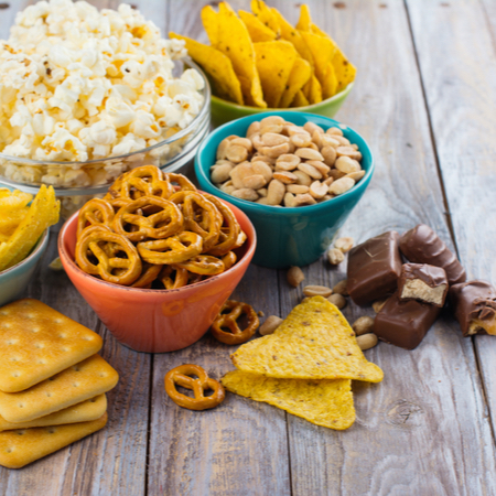 An array of snacks in bowls, including popcorn, chips, pretzels, chocolate and nuts