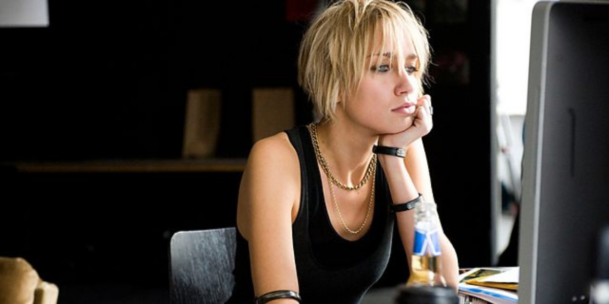 Image shows Frankie sitting at her computer wearing a black tank top and resting one of her hands under her chin.