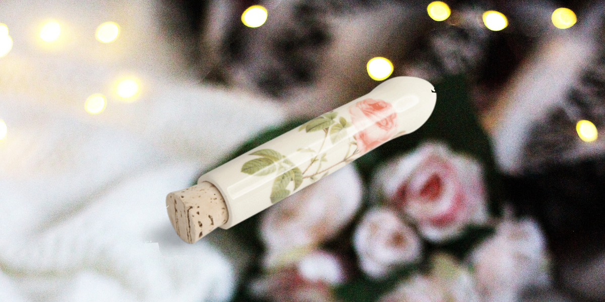 Image shows a ceramic dildo with a rose on it overlaid on a photo of roses and christmas lights