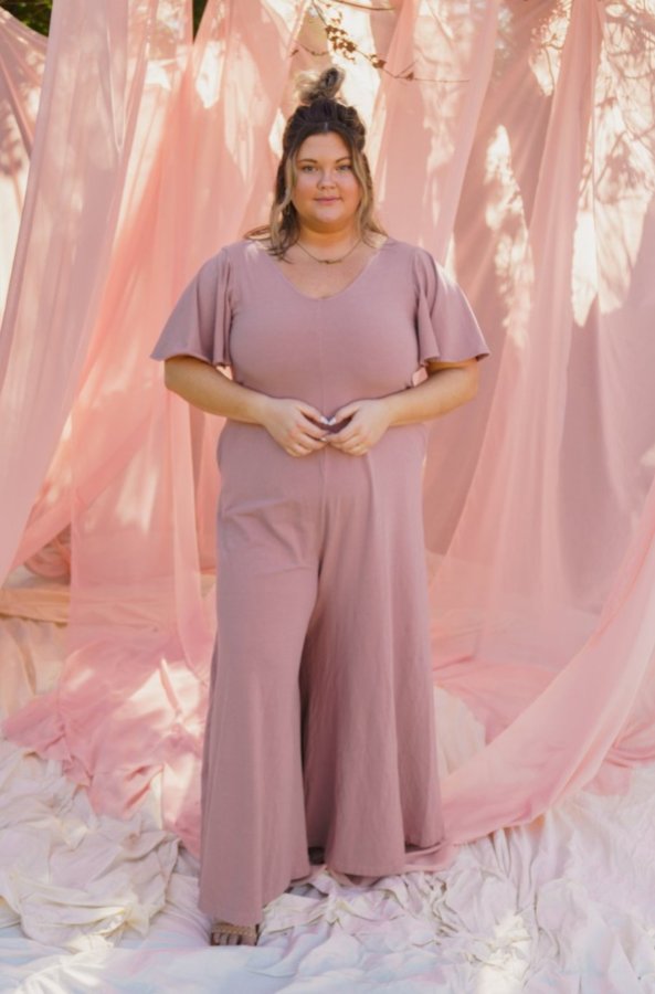 Holiday Lookbook For Fat Femmes: A person wearing a short sleeved pink jumpsuit