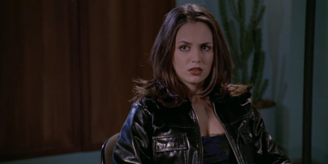 Image shows Faith sitting on a couch wearing a black leather jacket and giving an attitudinal face to the camera