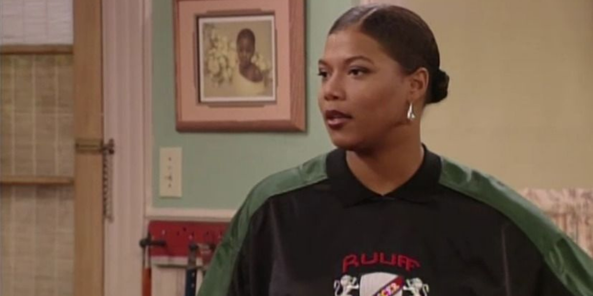 Image shows Khadijah, standing in a kitchen wearing an oversized jersey with her hair pulled back into a tight bun