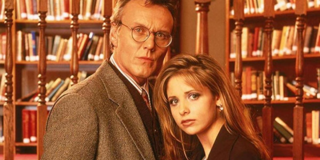 Buffy and Giles are standing in a library both looking directly into the camera and the image is sepia tones