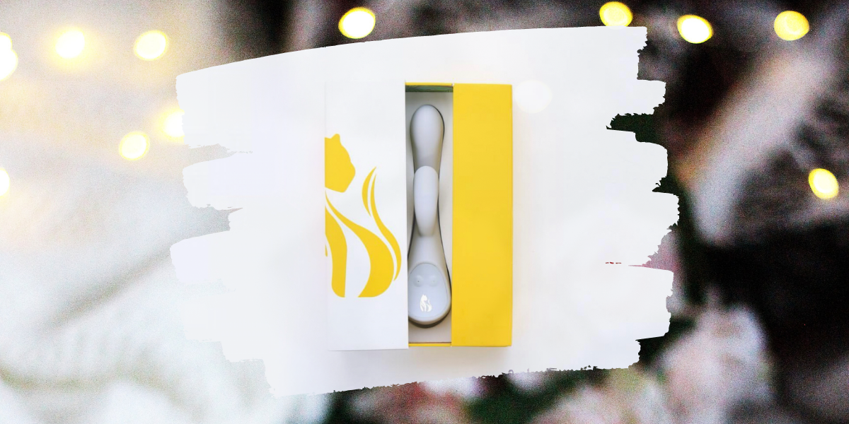 Sex toy gift guide: Image shows the lioness vibrator in gray, which has an external vibrating nub, inside it's box which is yellow and white and has an outlined image of a lion overlaid on a photo of roses and Christmas lights.