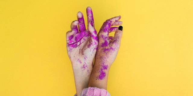 A photo of hands covered in purple glitter against a yellow background.