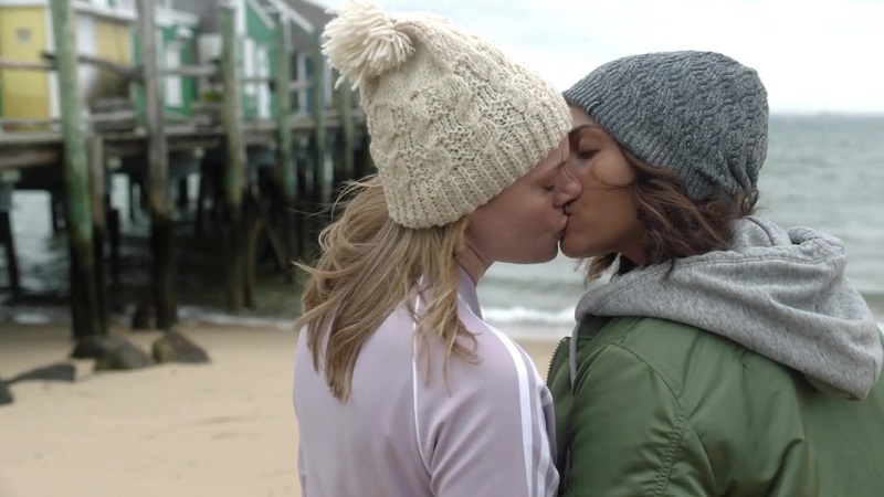 Leslie and Jackie hold hands and kiss on the beach.