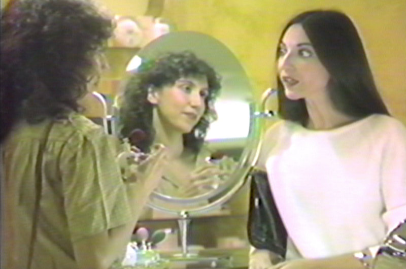 Two women speak at a perfume counter, one of them reflected in a mirror