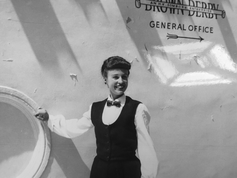Lisa Ben poses for a photo, which is in black and white, while wearing a tuxedo. She has a warm smile on her face.