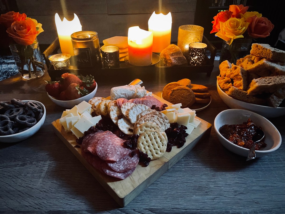 coffee table loaded with snacks, drinks, sweets, and a cheese board for holiday date night