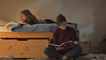 Petite Maman review: Joséphine Sanz as Nelly and Nina Meurisse as her mother read books together, Nelly on her bed, her mother on the floor next to her