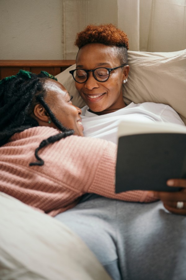 two smiling black queers reading together in bed