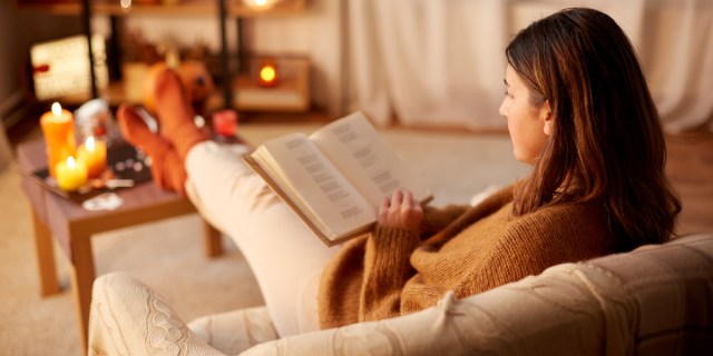 A woman reading in front of a cozy set of candles on a coffee table