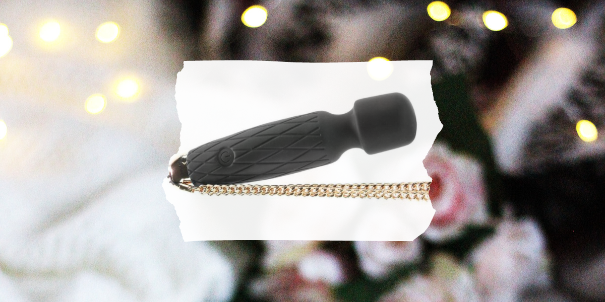 Image shows a small matte black wand vibrator with a gold link chain attached on the end overlaid on a photo of roses and Christmas lights.