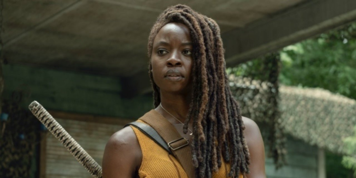 Image shows Michonne, A Black woman with thick locs to one side of her face, wearing an orange shirt with her Kitana on her back. Her expression is one of confusion and annoyance.