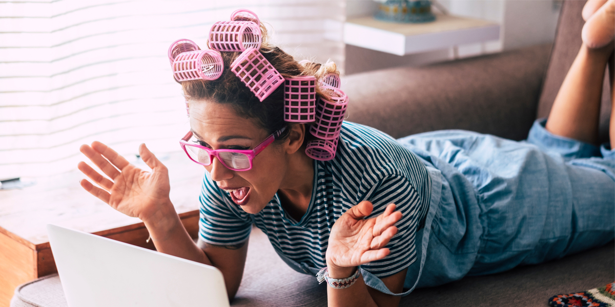 A woman in pink hair rollers makes a surprised face at her laptop screen