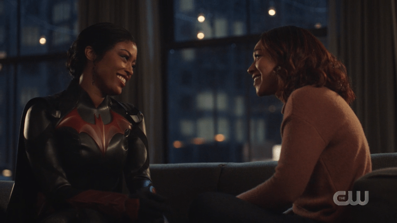 Ryan Wilder, dressed as Batwoman, and Iris West sitting on the couch smiling at each other.