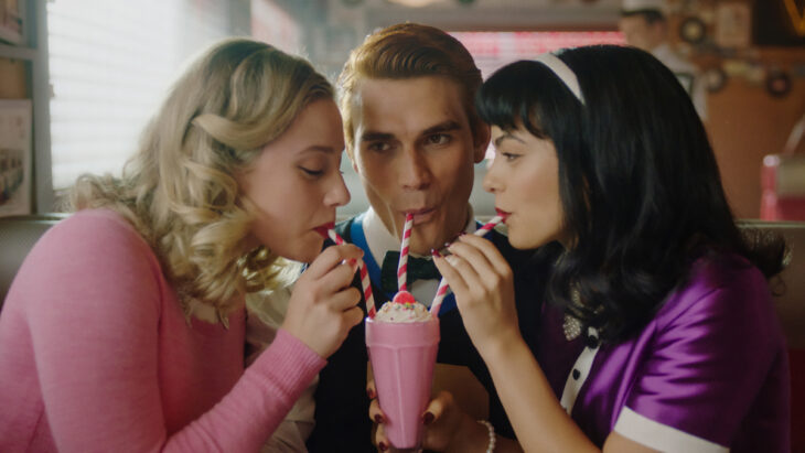 Betty, Archie, and Veronica from Riverdale sipping a milkshake