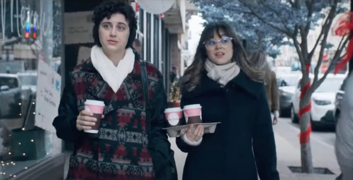 two characters from "Christmas is Cancelled" walking through the snow with coffee