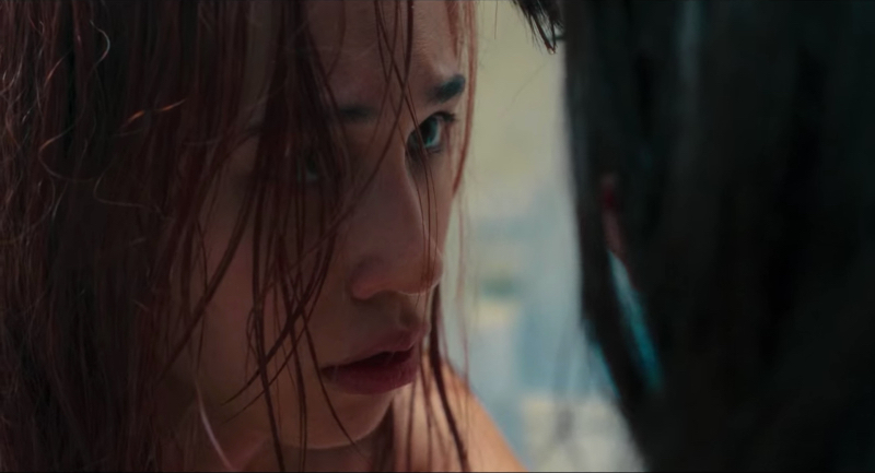 A close up on Kiko Mizuhara, wet red hair covering one eye as she looks at another woman.