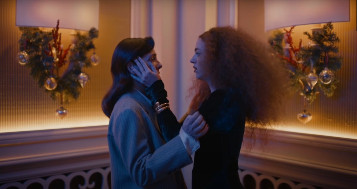 Two fancy women holding each other's faces like they're about to kiss