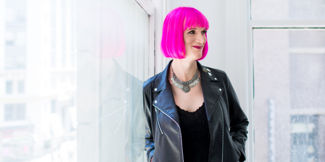Charlie Jane Anders interview: A photo of the author Charlie Jane Anders with a pink bob, wearing a leather jacket and black top