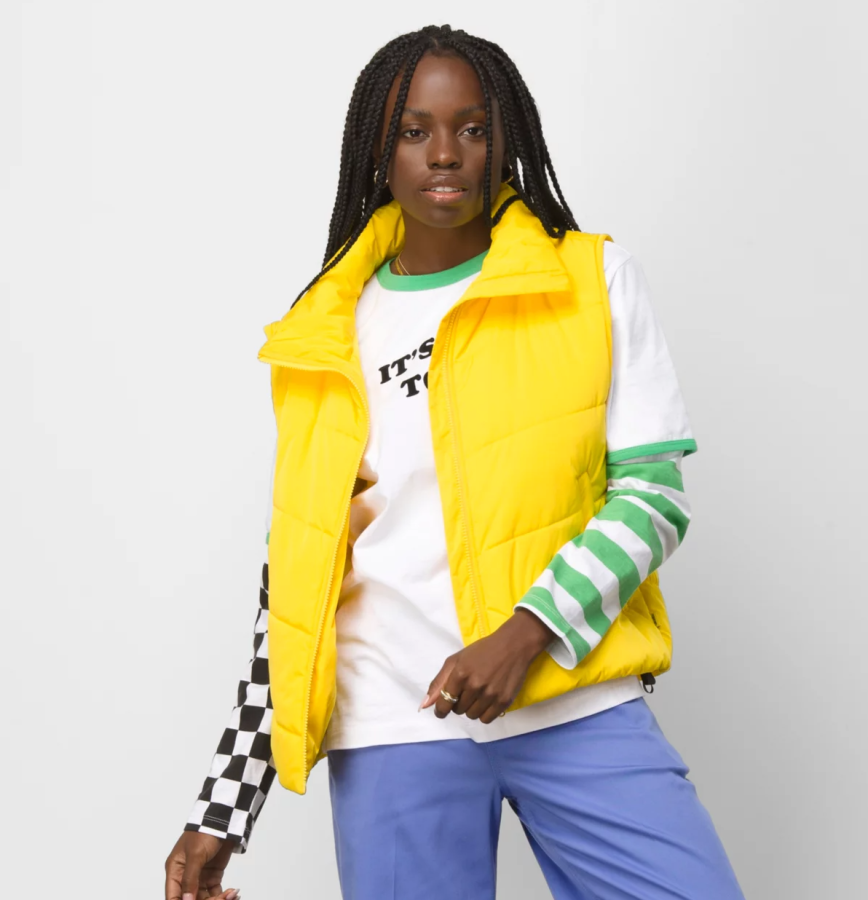 A person wearing a yellow puffer vest over a long sleeved shirt and blue pants