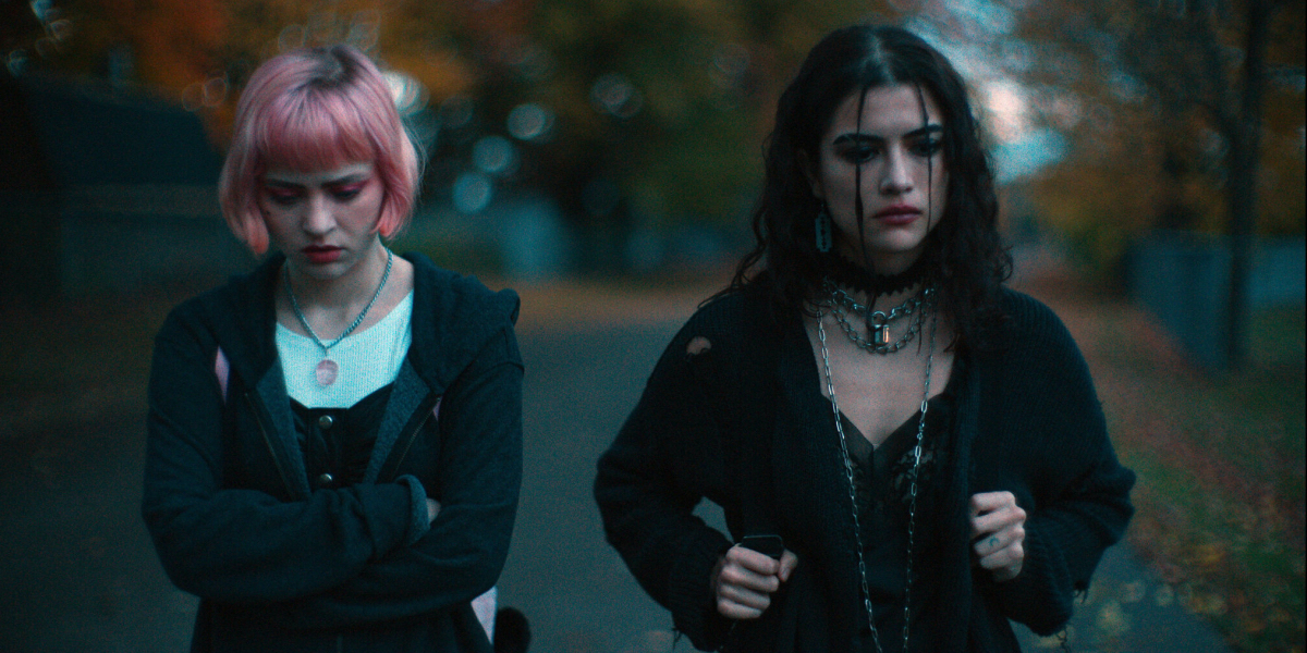 A still from We Need to Do Something: Sierra McCormick with pink hair and Lisette Alexis as goth walk on a fall day