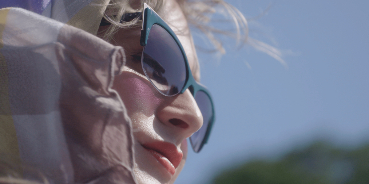 A close up of Zackary Drucker as Agnes wearing sunglasses and a scarf around her head.