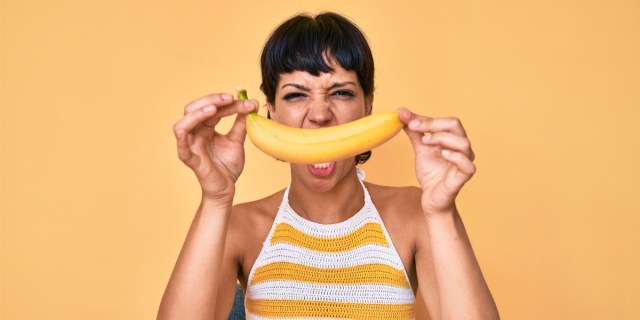 A woman holds a banana in front of her face while being mad