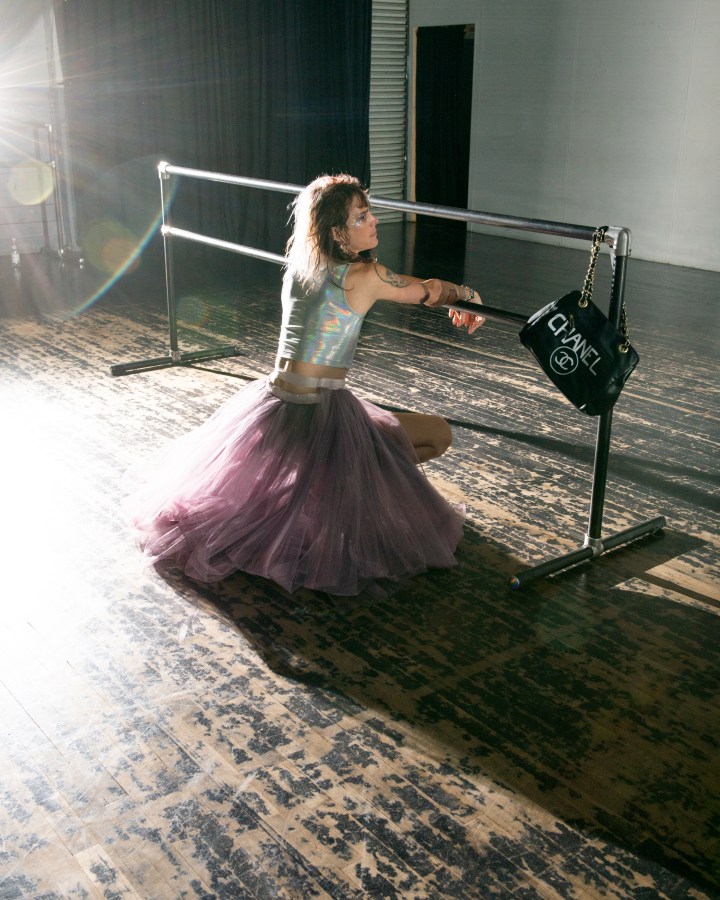 CJ Kitten Miller, the author of this essay, poses in a long purple tulle skirt and a shiny tank top. Her hair is pink and her heels are high. Four in a series of five.