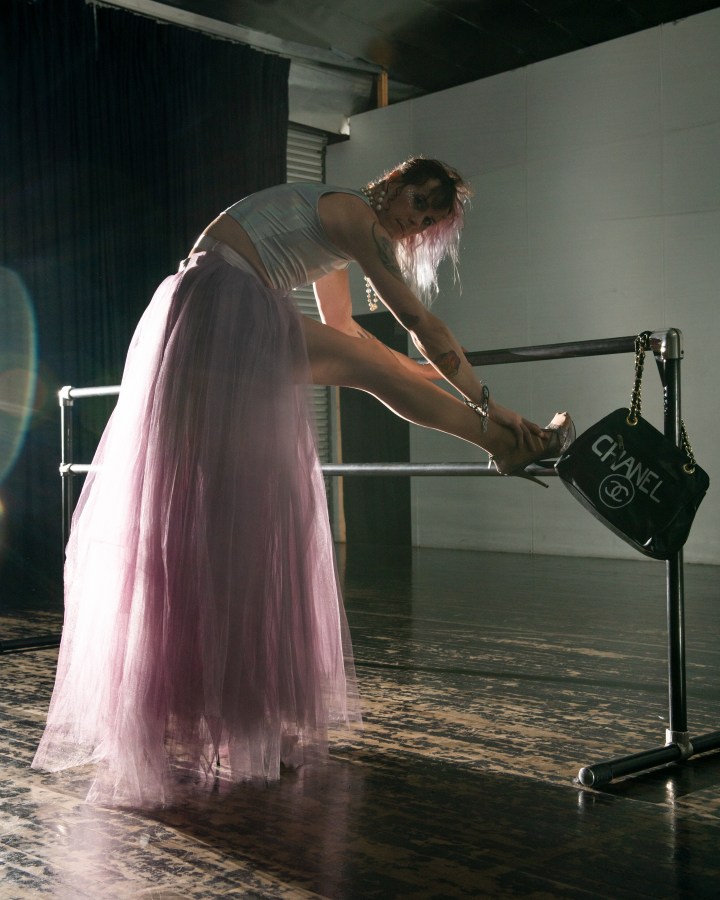 CJ Kitten Miller, the author of this essay, poses in a long purple tulle skirt and a shiny tank top. Her hair is pink and her heels are high. One in a series of five.