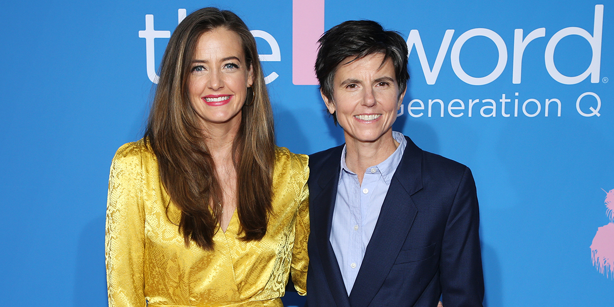 Tig Notaro in a blue suit and Tig Notaro and Stephanie Allynne in a gold dress stand arm in arm on the red carpet at The L Word: Generation Q season two premiere