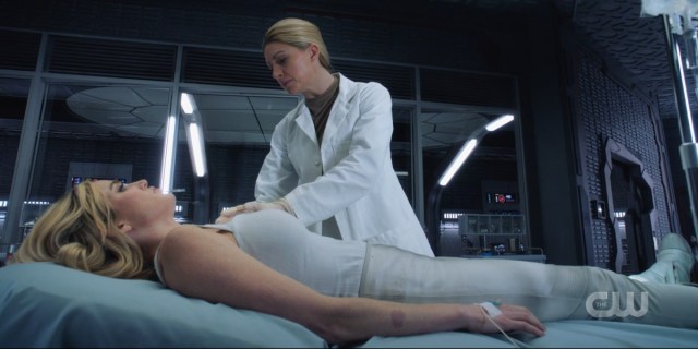 Ava stands over Sara in a white lab coat