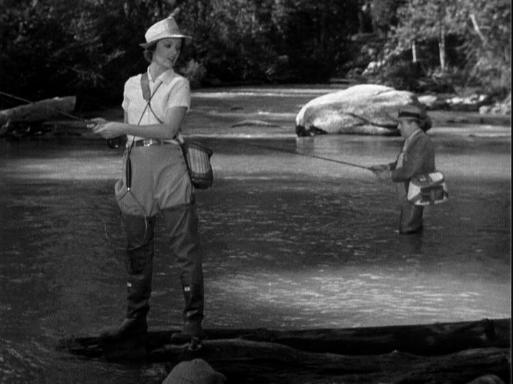 A screenshot of Myrna Loy in Libeled Lady, holding a fishing pole in a body of water