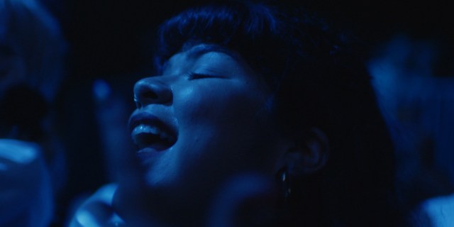 Close-up of Doris Muñoz's face in dark blue lighting. She is looking up with her mouth open as she dances.