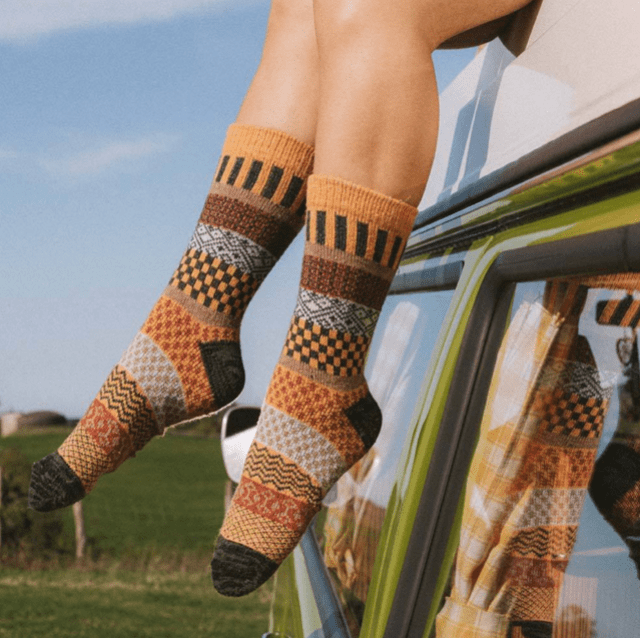 A woman's shapely legs in brown colorful wool socks. She's hanging out of a car window.