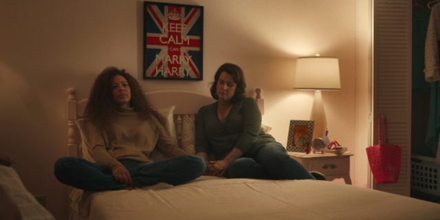 Yellowjackets 108 screencap: Adult Taissa and Adult Shauna sitting on a bed, holding hands