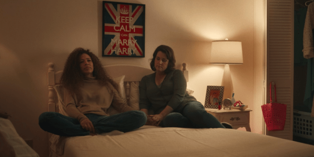 Yellowjackets 108 screencap: Adult Taissa and Adult Shauna sitting on a bed, holding hands
