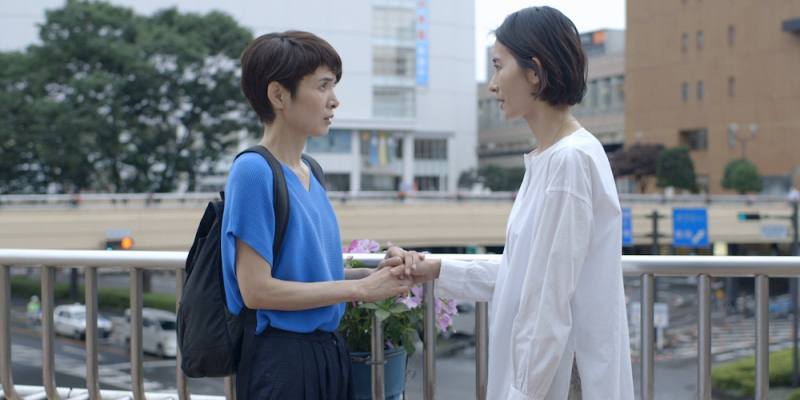 Fusako Urabe and Aoba Kawai stand on an elevated train platform holding hands.