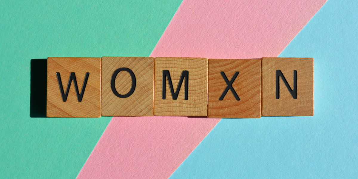 The word "womxn" is spelled out in scrabble letters, against a green, pink, and blue background