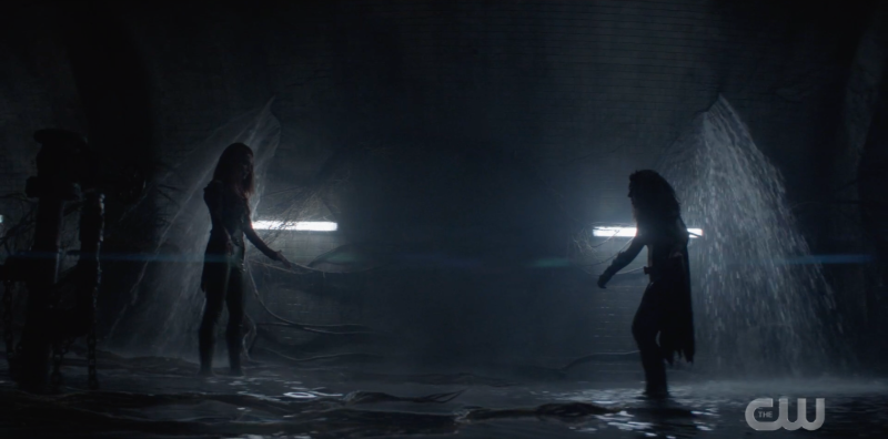 Batwoman and Pam stand facing each other under the dam, ready to fight.