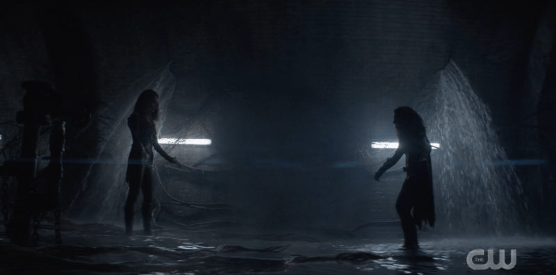 Batwoman and Pam stand facing each other under the dam, ready to fight.