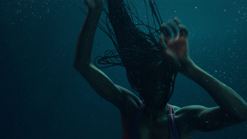 A woman reaches up her arms drowning in dark water.